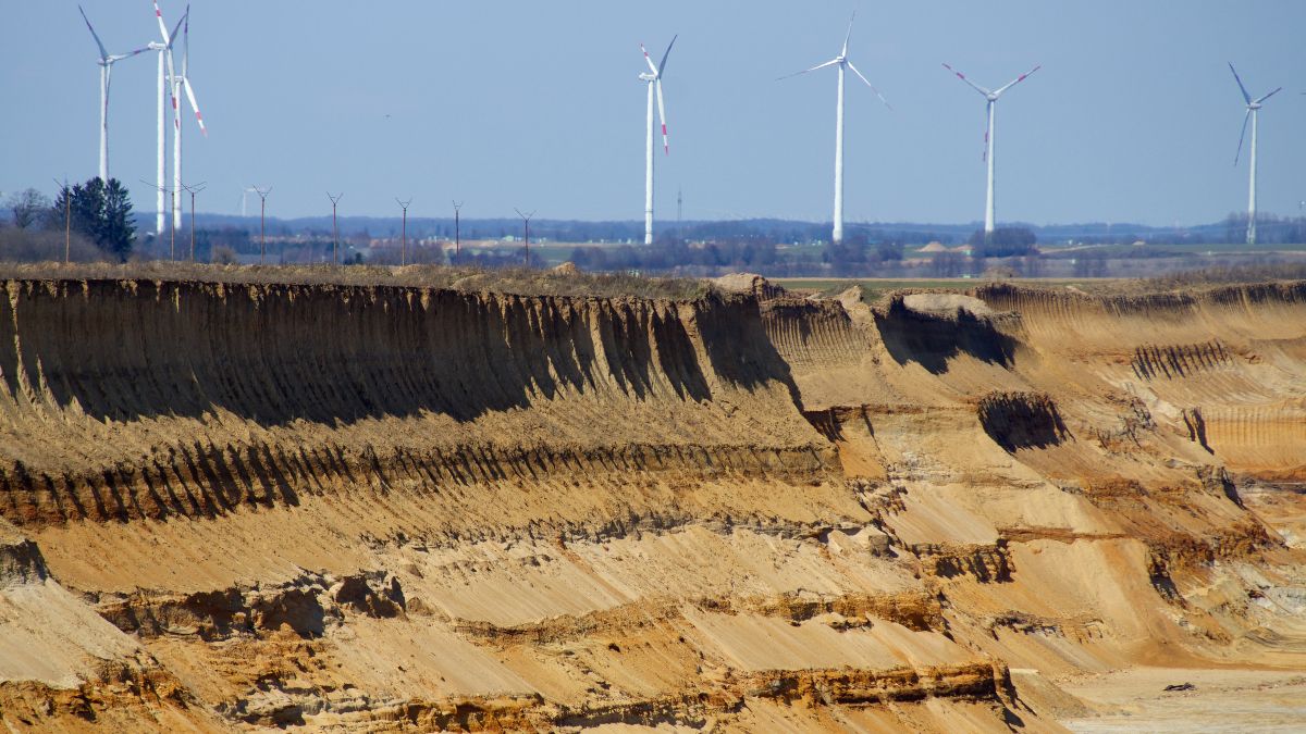 Sandige Böschung am Tagebaurand mit Windrädern im Hintergrund