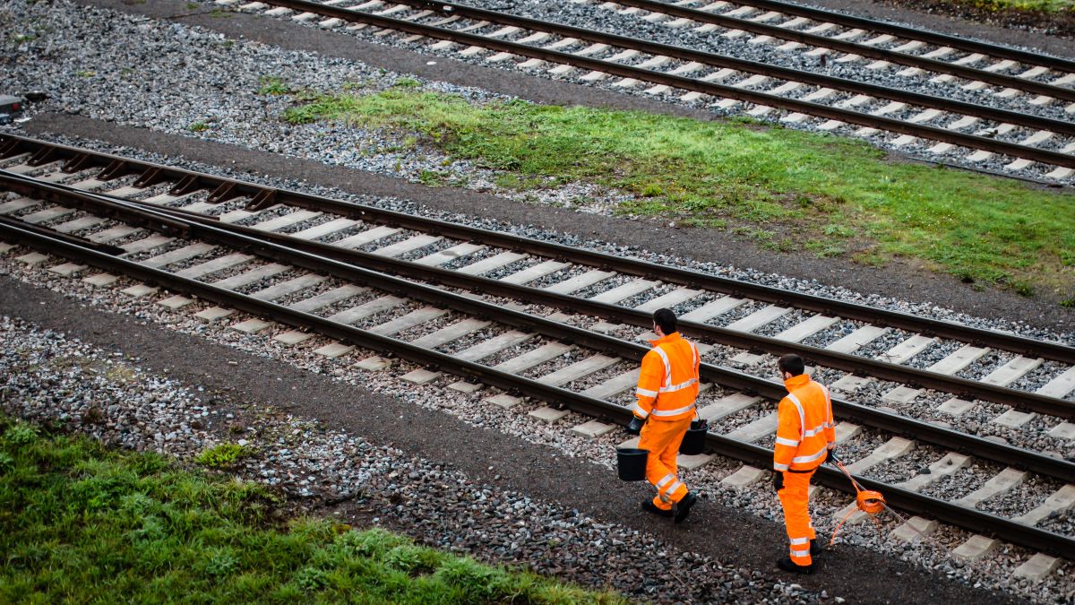 zwei Arbeiter in orangefarbenen Signalanzügen gehen an Schienen entlang